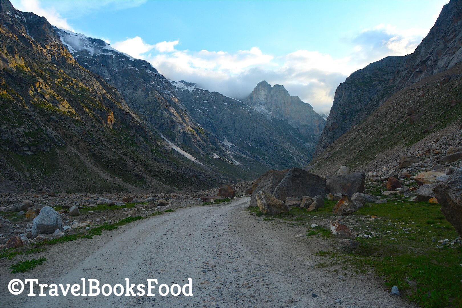 A gravel road in the middle of many mountains and some huge rocks