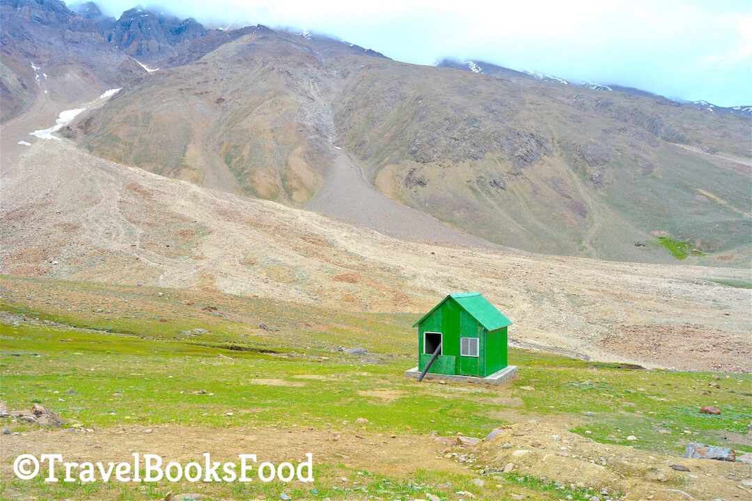 A green shed surrounded by mountains in a vast green field