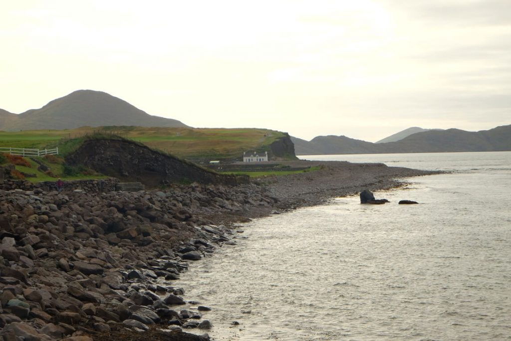 A picture of a shore with black rocks and hills in the distance
