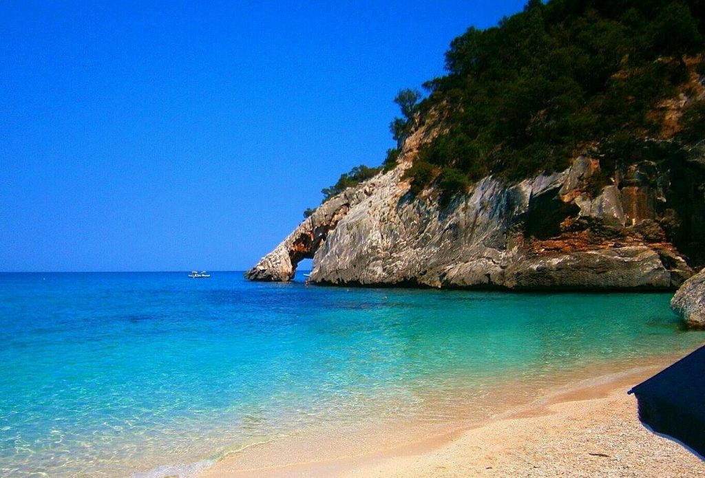 A photo of a white beach with blue-green water and some cliffs in the background