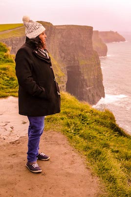 A photo of Soumya Nambiar, a well known Indian travel blogger staring into the distance at the Cliffs of Moher in Ireland